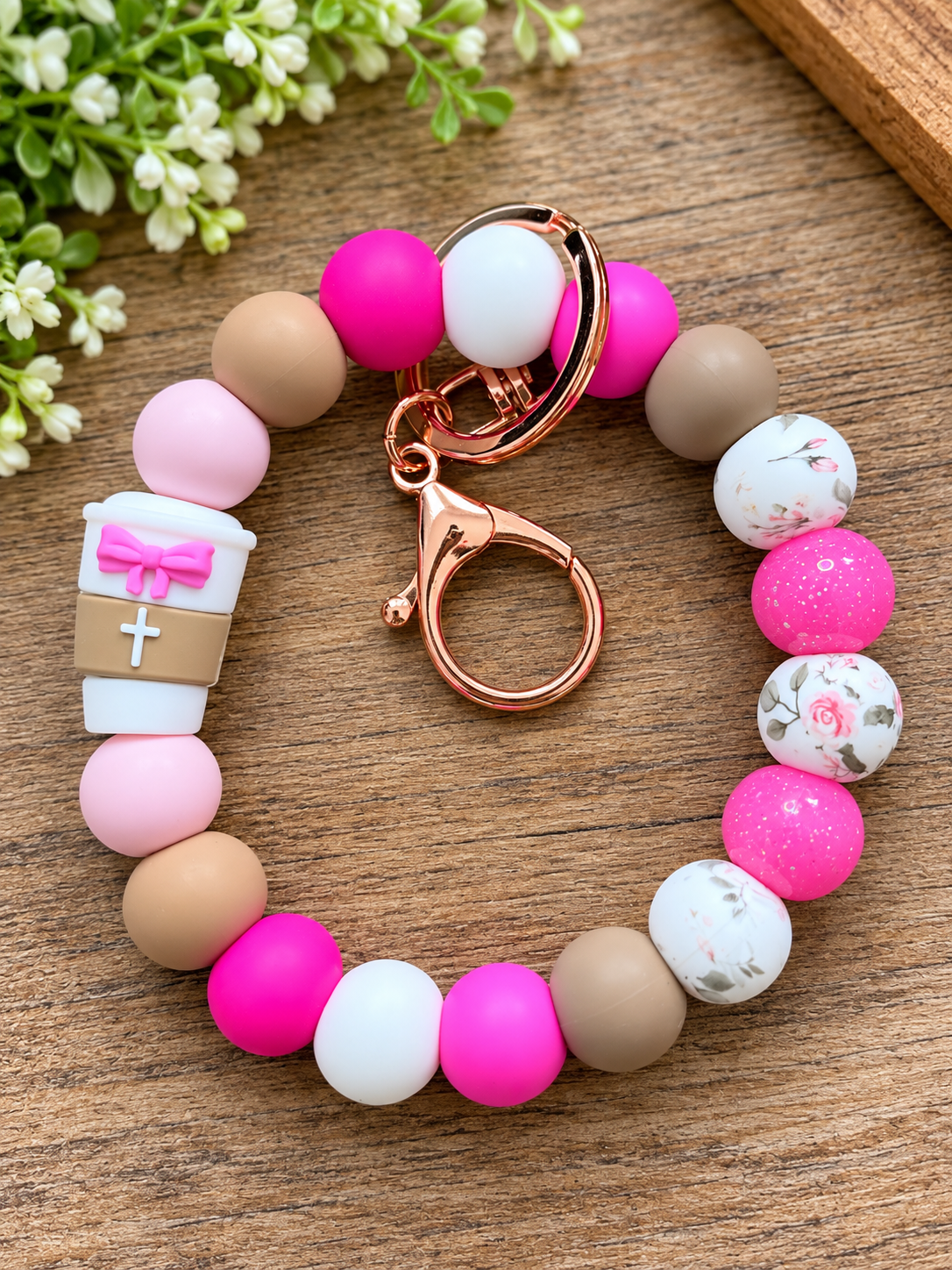 Close-up of a pink floral silicone bead wristlet design with a coffee cup focal featuring a pink bow and white cross, coordinating matte beads, glitter beads, and lobster claw keychain.