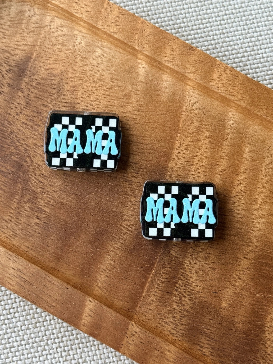 Checkered Mama acrylic focal bead with bright blue MAMA lettering over a black and white checkerboard design, sold individually for beaded crafts.