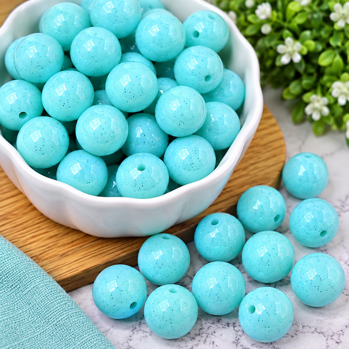 Aqua blue round beads with a subtle sparkle finish and center holes, styled in a glass dish for jewelry making, keychains, wristlets, and craft projects.
