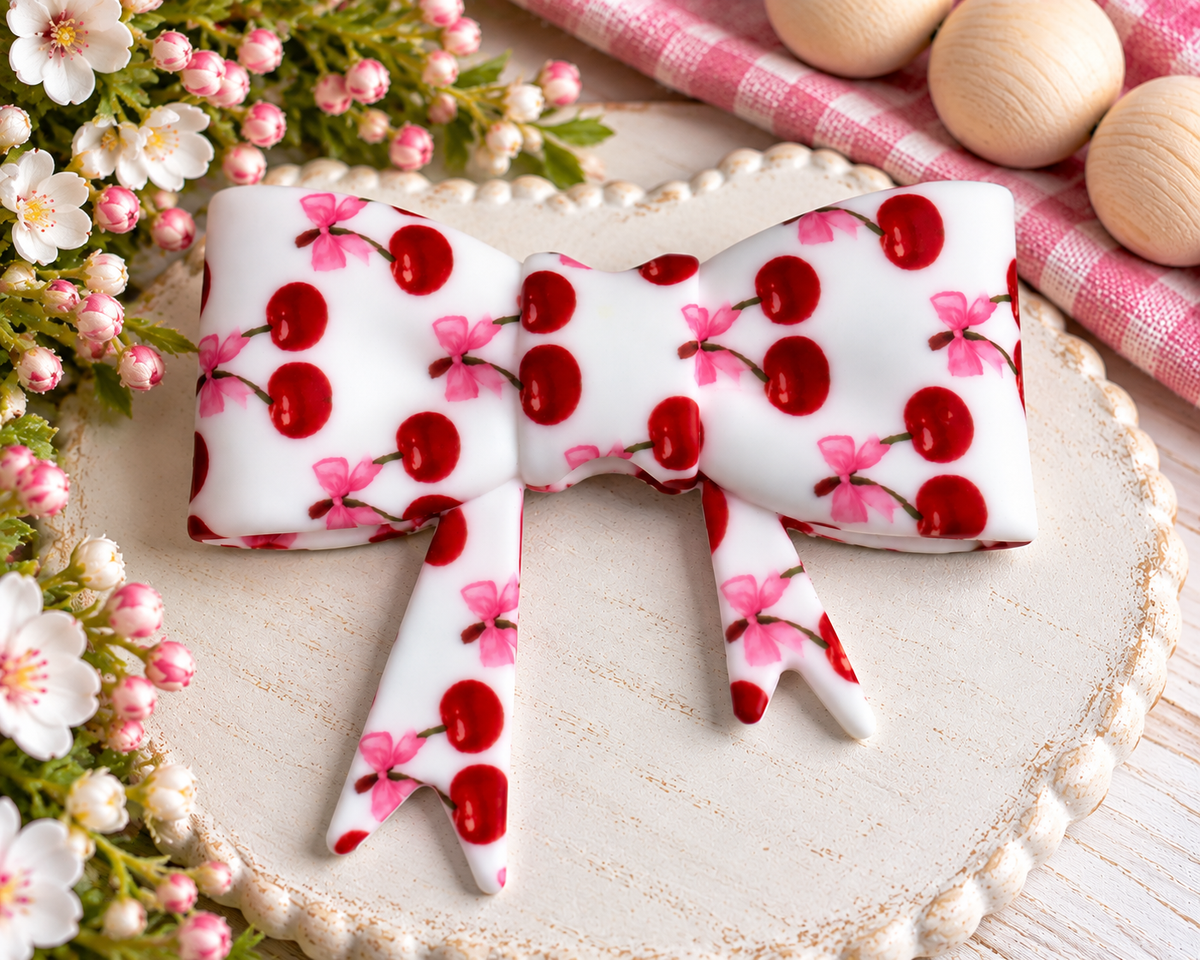 Large white silicone bow focal bead featuring bright red cherries and pink bow accents for wristlets, bag charms, keychains and DIY beading.