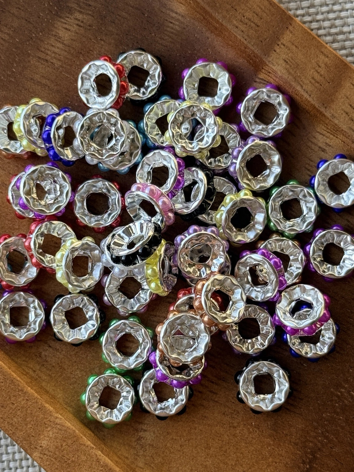 Colorful pearl wide hole spacer beads with shiny silver accents in assorted colors, displayed in a wooden tray for jewelry and craft projects.