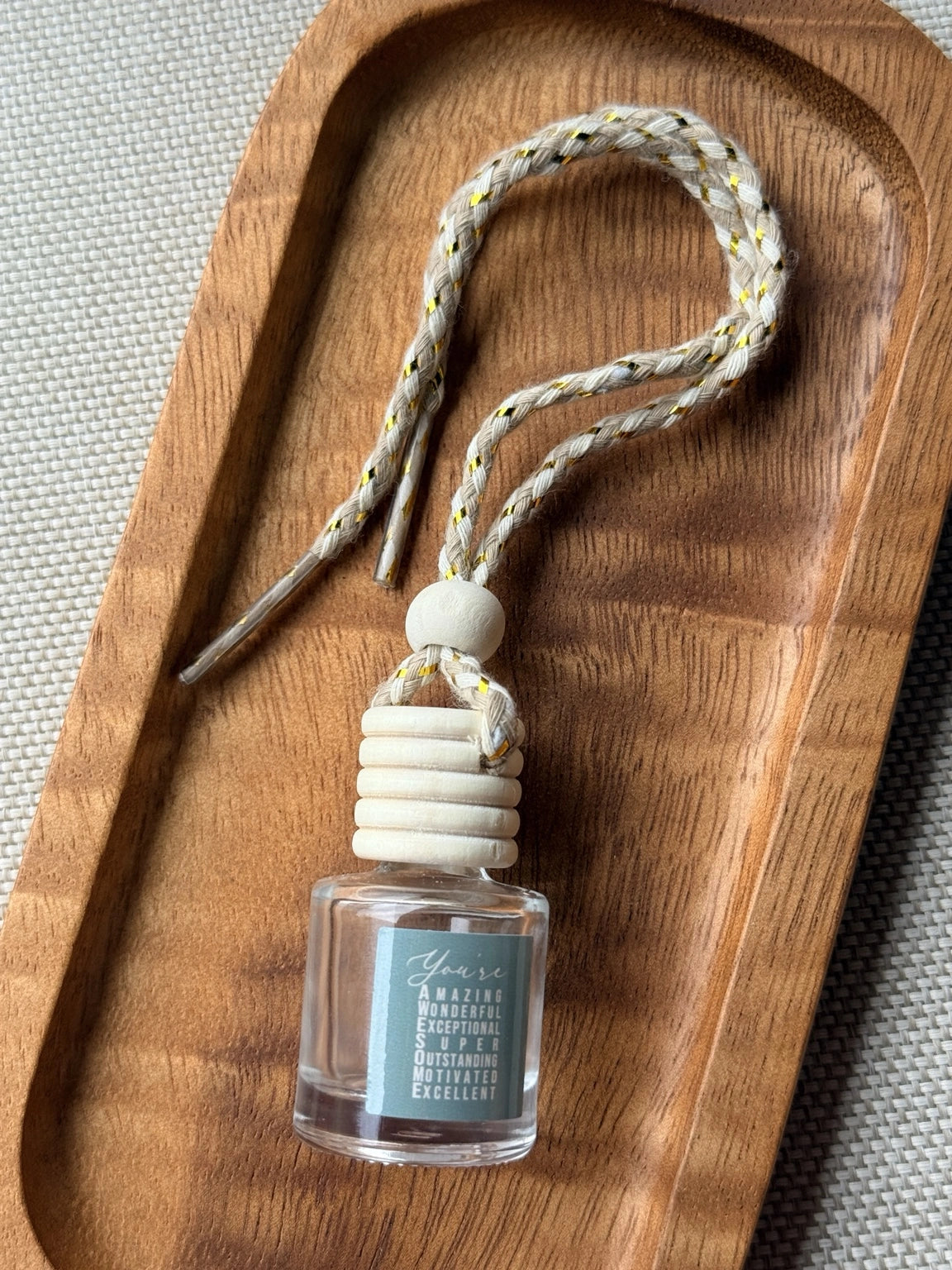 Empty refillable glass and wood hanging car diffuser bottle by Four Seasons of Happiness with natural wooden cap, decorative hanging cord, and colorful “You’re Awesome” label. Holds your favorite fragrance or essential oil and is sold individually.