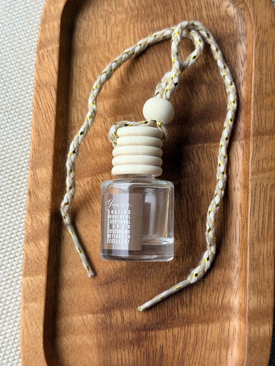 Empty refillable glass and wood hanging car diffuser bottle by Four Seasons of Happiness with natural wooden cap, decorative hanging cord, and colorful “You’re Awesome” label. Holds your favorite fragrance or essential oil and is sold individually.