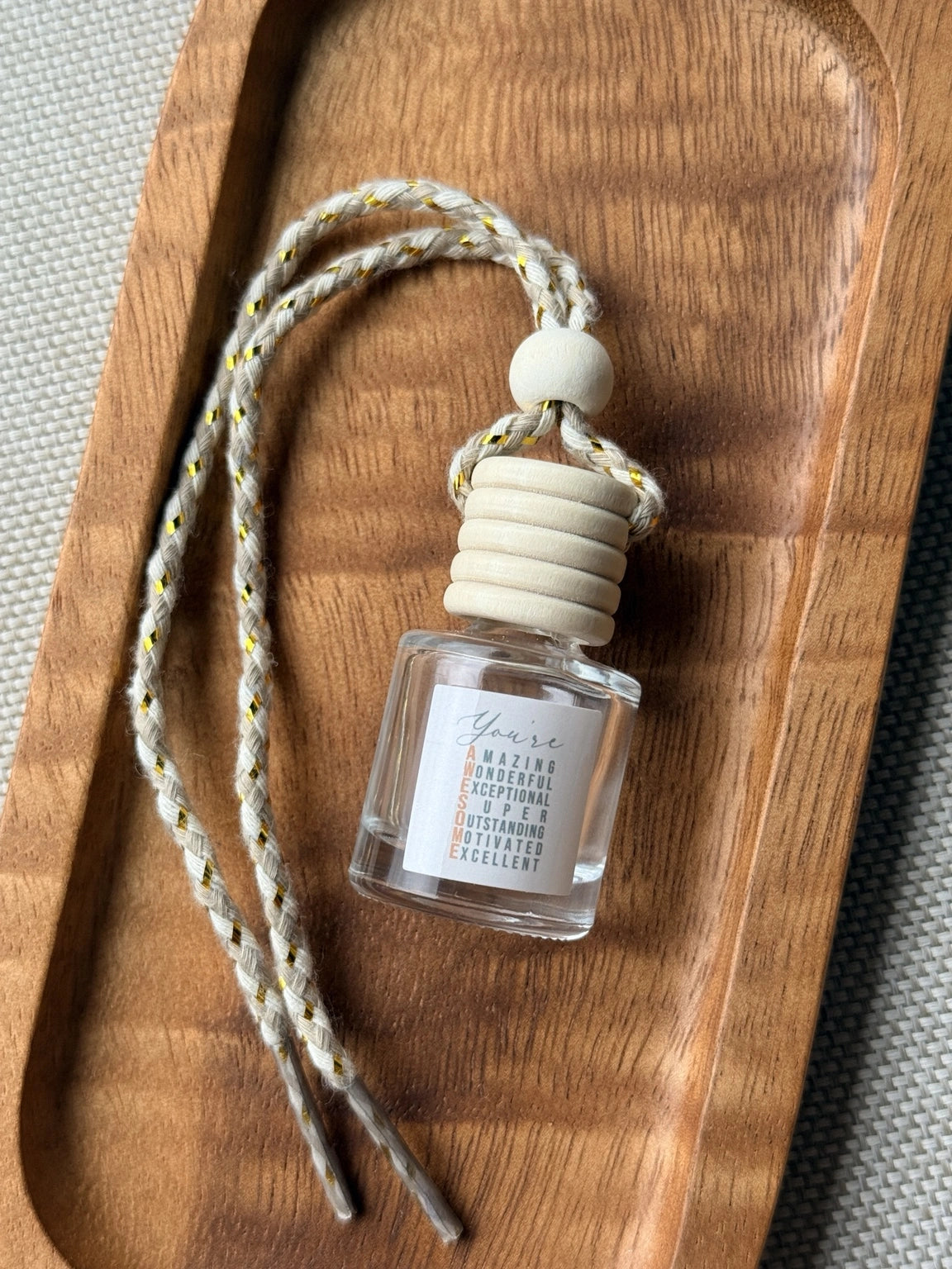 Empty refillable glass and wood hanging car diffuser bottle by Four Seasons of Happiness with natural wooden cap, decorative hanging cord, and colorful “You’re Awesome” label. Holds your favorite fragrance or essential oil and is sold individually.
