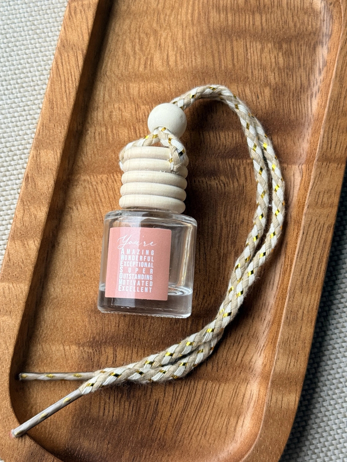 Empty refillable glass and wood hanging car diffuser bottle by Four Seasons of Happiness with natural wooden cap, decorative hanging cord, and colorful “You’re Awesome” label. Holds your favorite fragrance or essential oil and is sold individually.