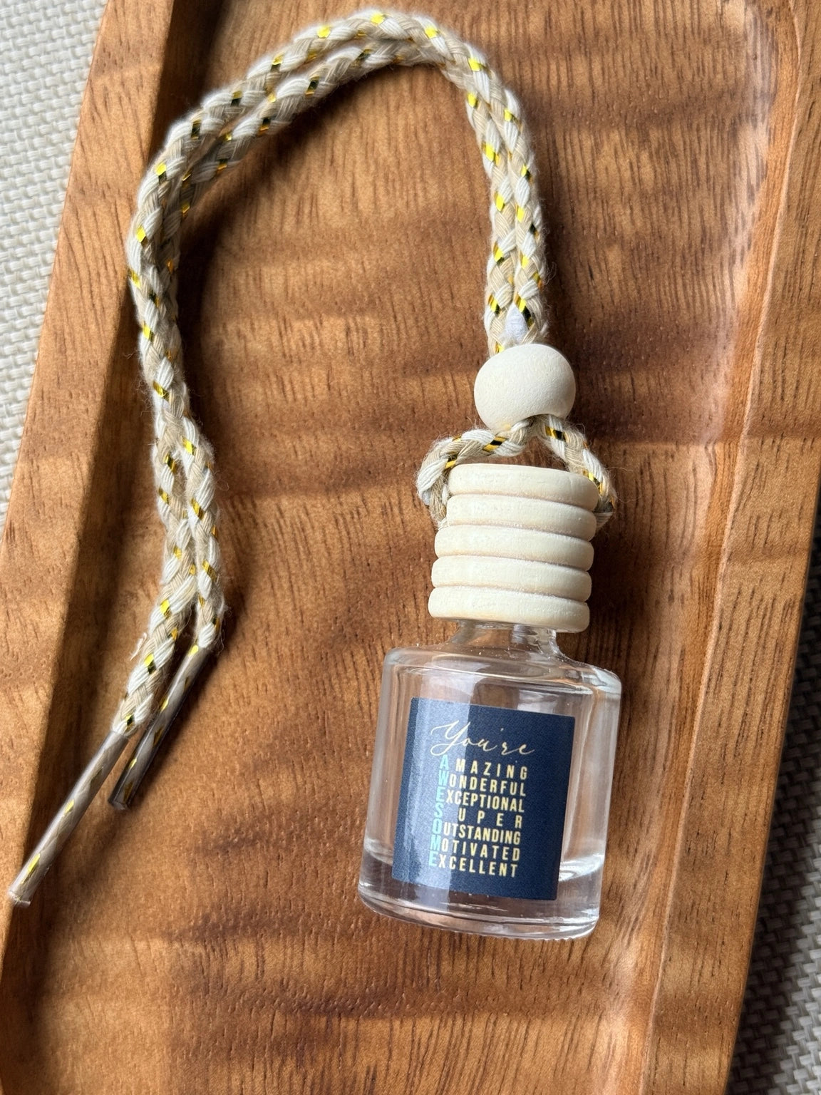Empty refillable glass and wood hanging car diffuser bottle by Four Seasons of Happiness with natural wooden cap, decorative hanging cord, and colorful “You’re Awesome” label. Holds your favorite fragrance or essential oil and is sold individually.