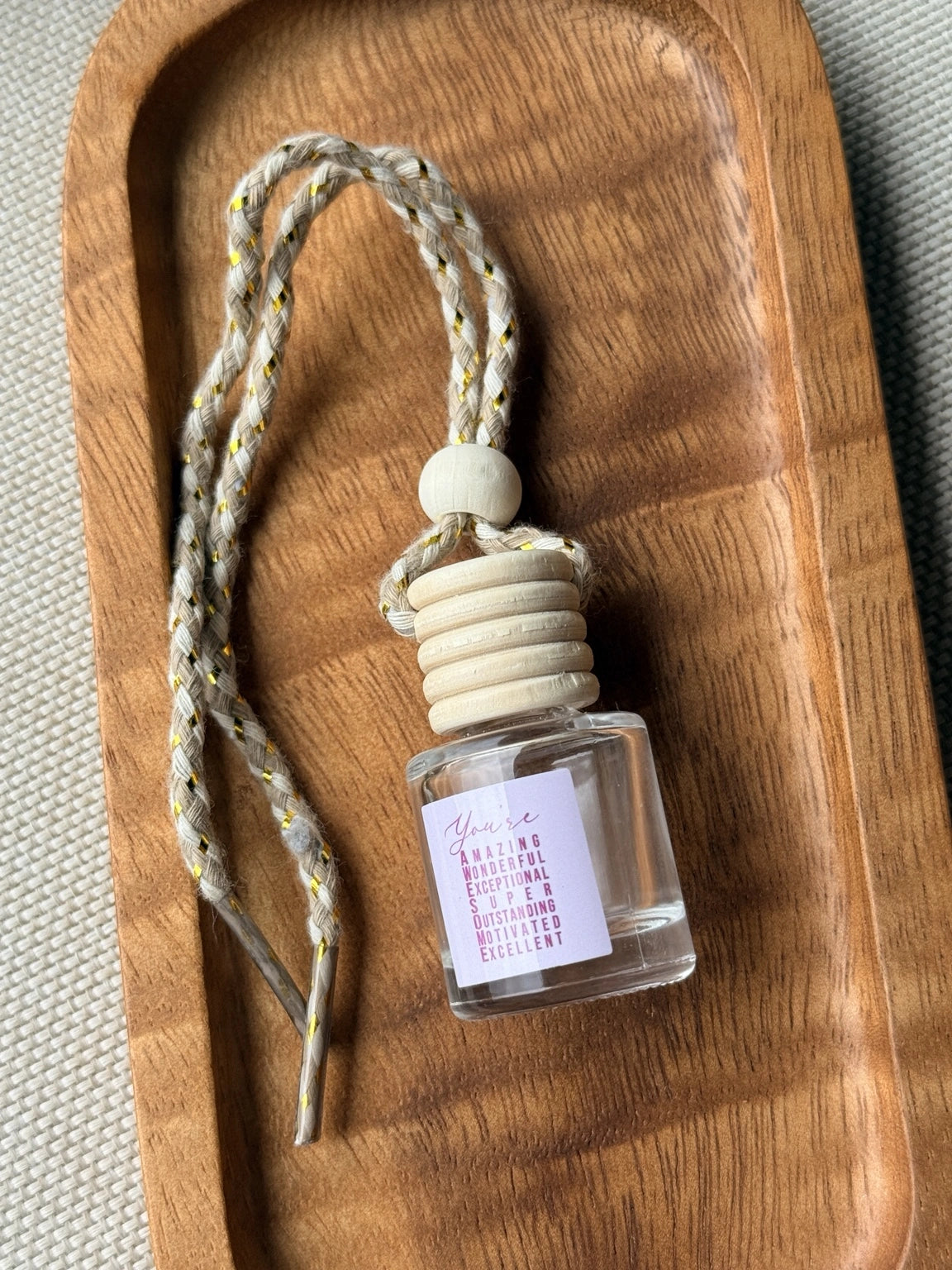 Empty refillable glass and wood hanging car diffuser bottle by Four Seasons of Happiness with natural wooden cap, decorative hanging cord, and colorful “You’re Awesome” label. Holds your favorite fragrance or essential oil and is sold individually.