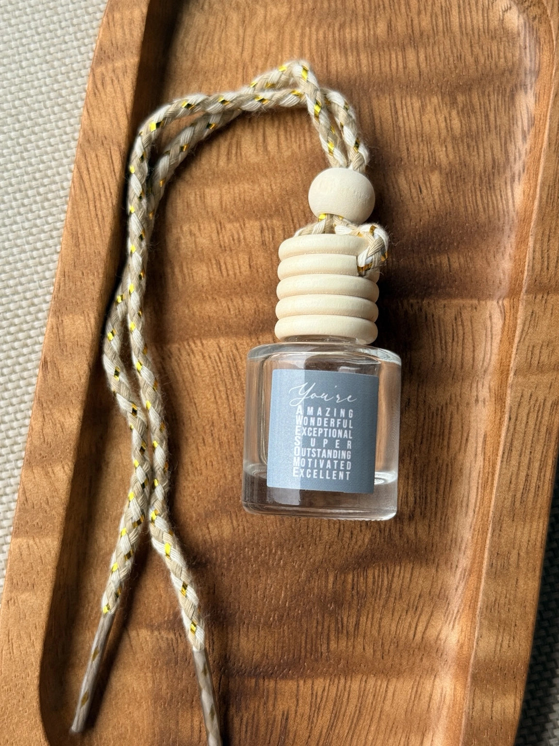 Empty refillable glass and wood hanging car diffuser bottle by Four Seasons of Happiness with natural wooden cap, decorative hanging cord, and colorful “You’re Awesome” label. Holds your favorite fragrance or essential oil and is sold individually.