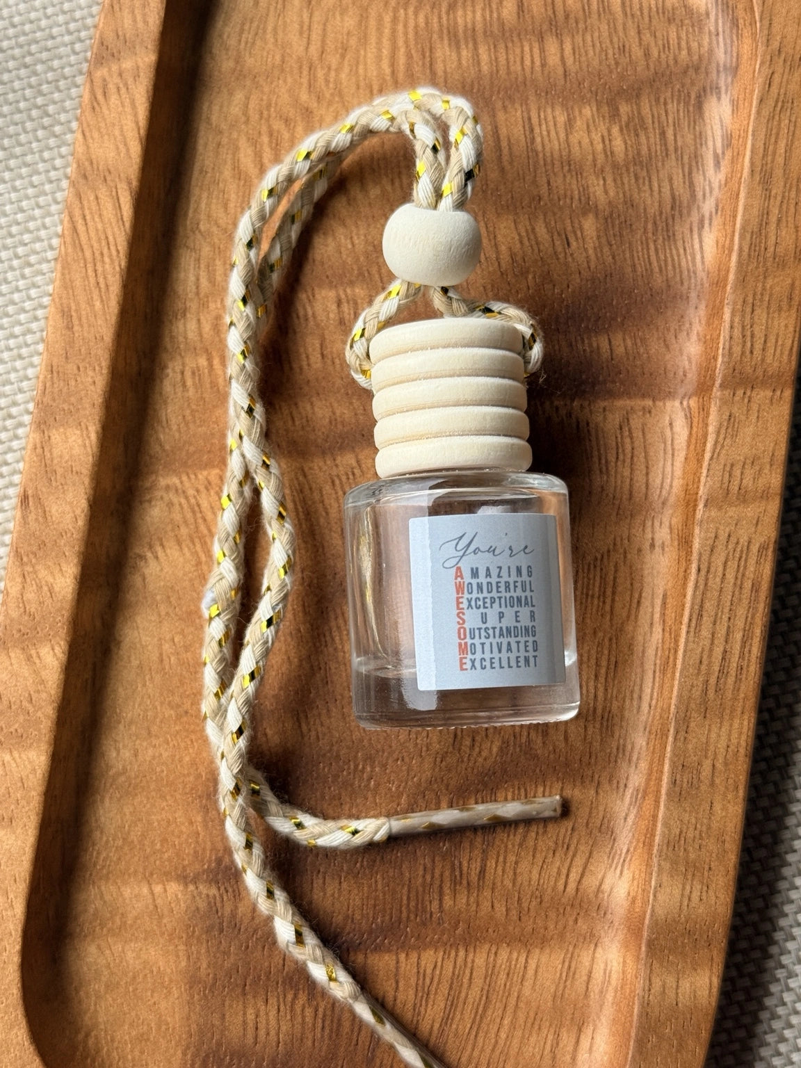 Empty refillable glass and wood hanging car diffuser bottle by Four Seasons of Happiness with natural wooden cap, decorative hanging cord, and colorful “You’re Awesome” label. Holds your favorite fragrance or essential oil and is sold individually.