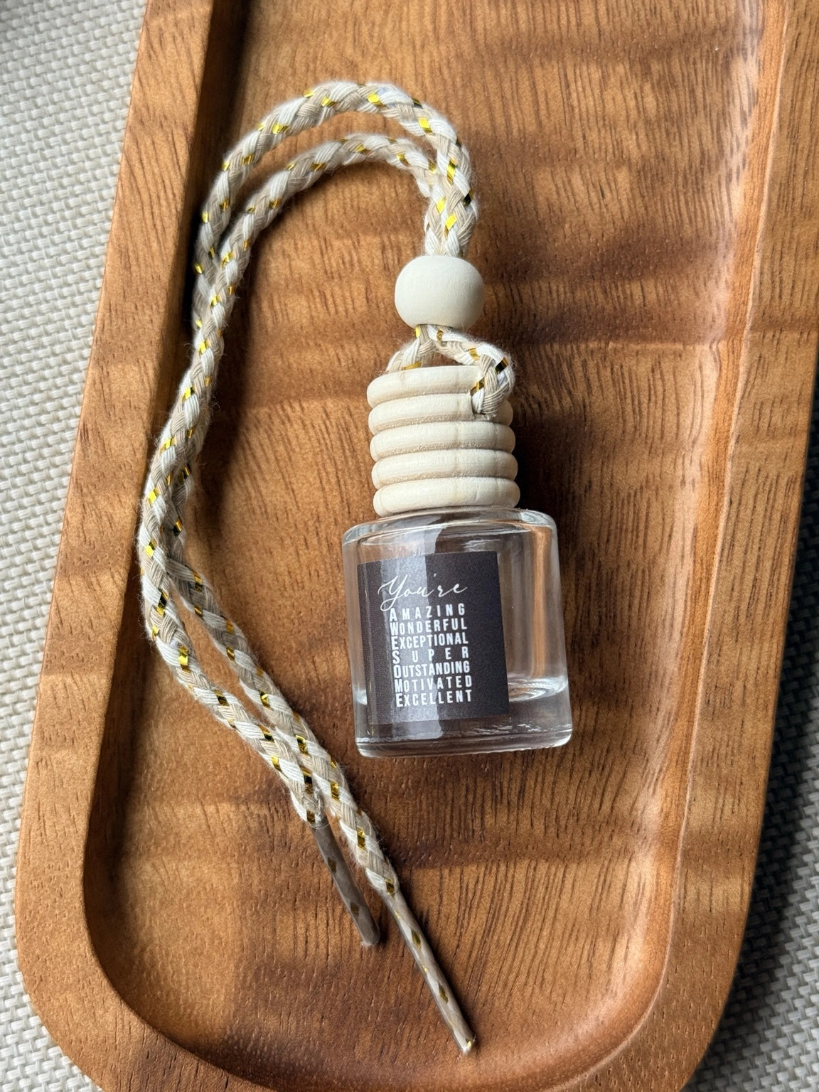 Empty refillable glass and wood hanging car diffuser bottle by Four Seasons of Happiness with natural wooden cap, decorative hanging cord, and colorful “You’re Awesome” label. Holds your favorite fragrance or essential oil and is sold individually.