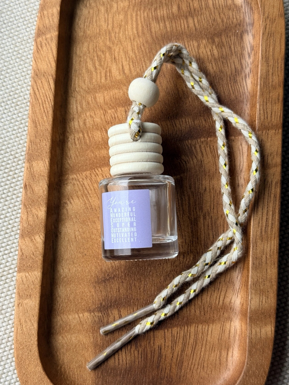 Empty refillable glass and wood hanging car diffuser bottle by Four Seasons of Happiness with natural wooden cap, decorative hanging cord, and colorful “You’re Awesome” label. Holds your favorite fragrance or essential oil and is sold individually.
