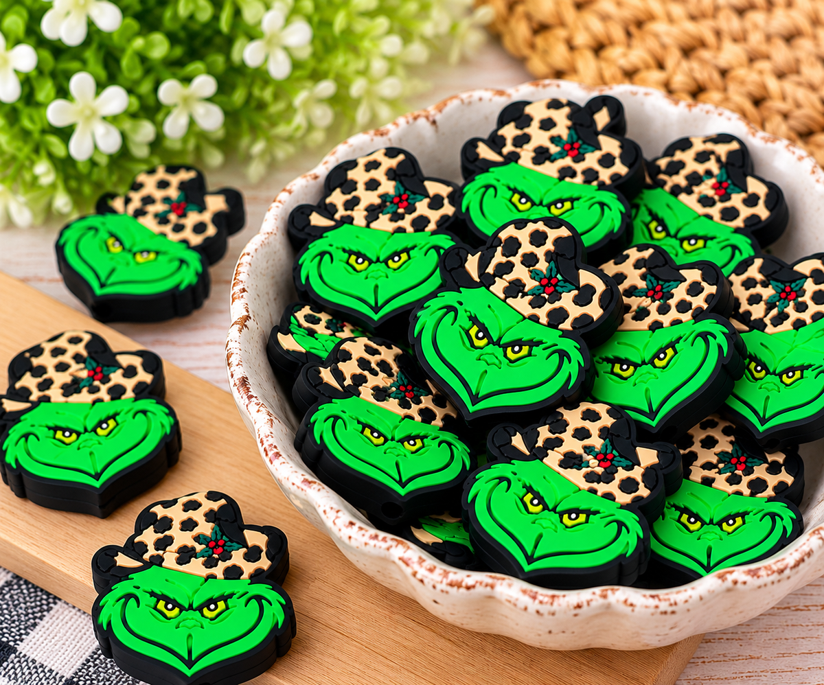 Close-up of green holiday character silicone focal beads with black outlines, leopard-print hats, and holly accents
