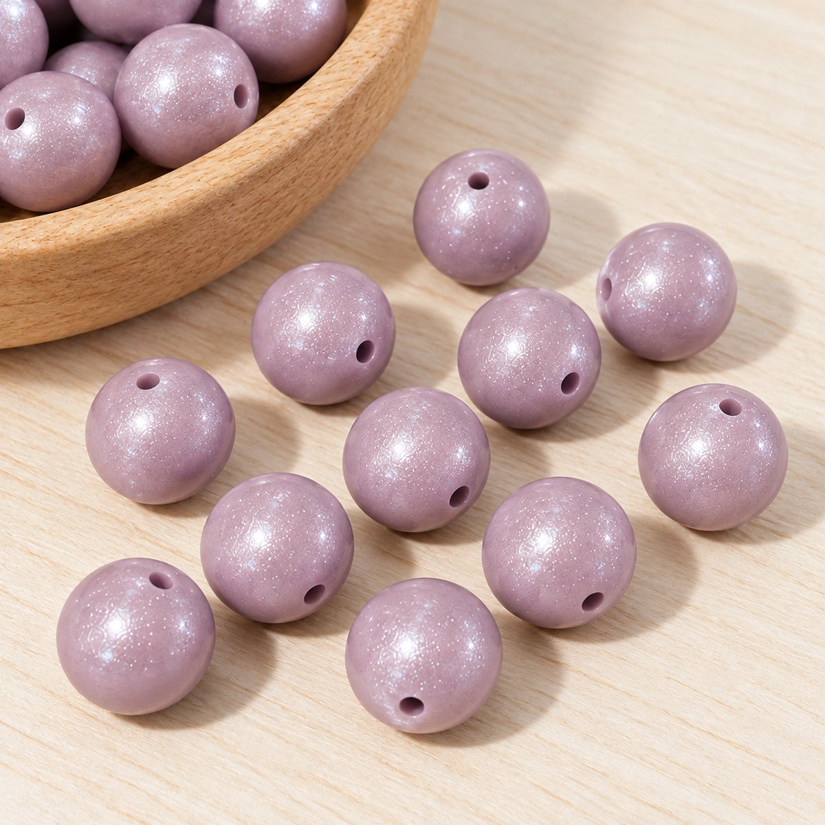 Close-up of lilac 15mm opal silicone beads on a light wooden surface, showing their pearlescent finish and threading holes.