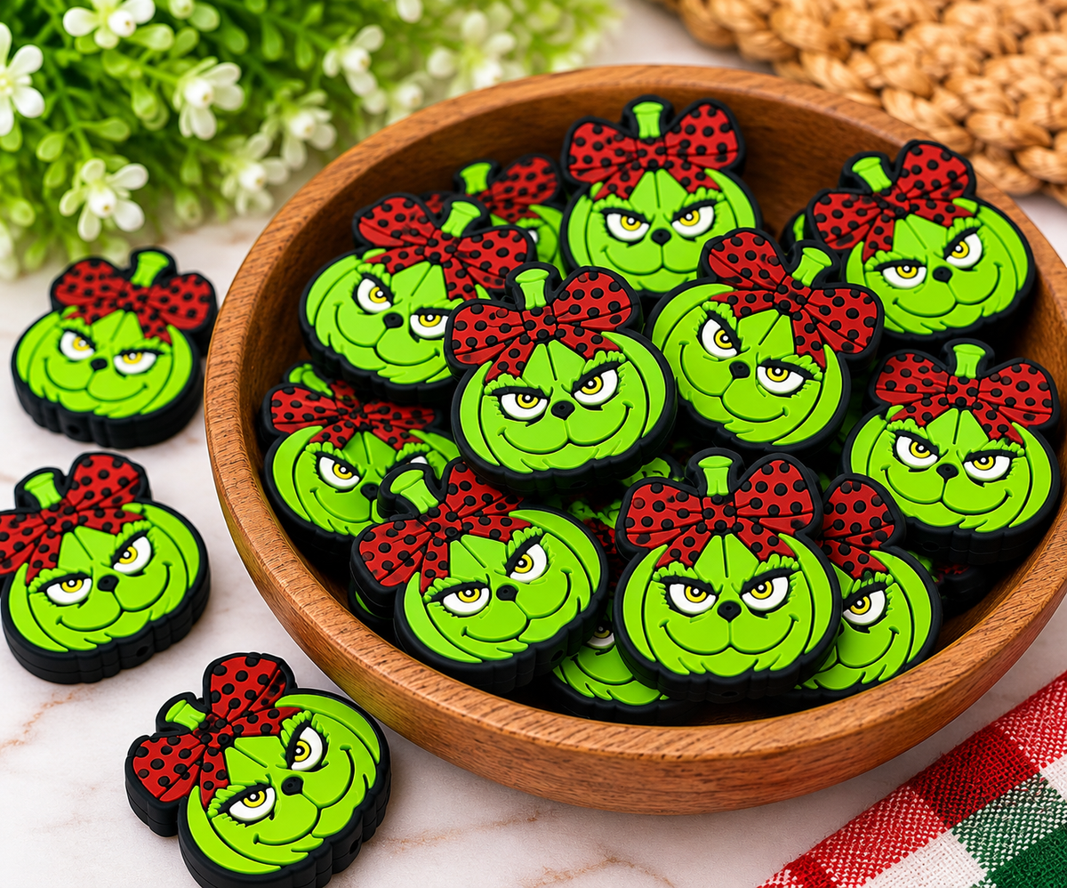Green holiday silicone focal beads featuring mischievous smiling faces and brown polka-dot bows, displayed on a wooden tray