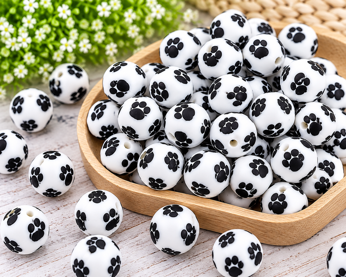 Close-up of black and white paw print 15mm silicone beads with round shape and through-holes for beading projects.