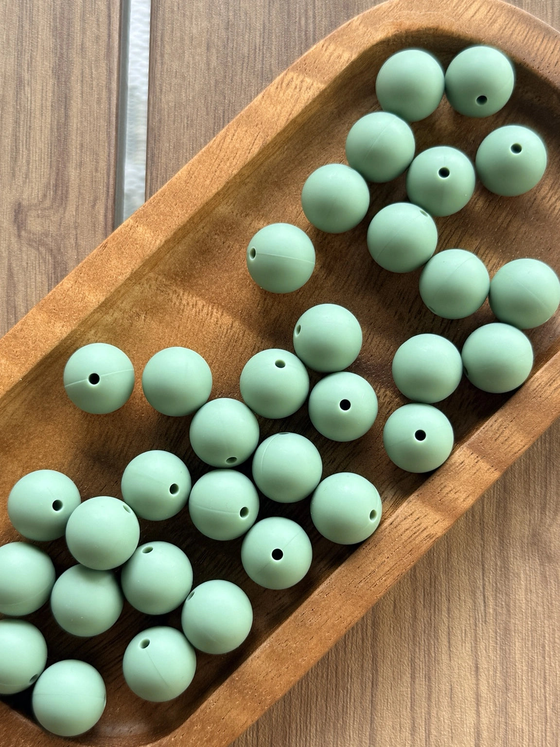 Muted eucalyptus green 15mm matte silicone round beads displayed on a wooden tray for beadable pens, jewelry making, wristlets, and DIY craft projects by Four Seasons of Happiness