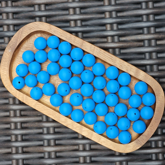 Blue Horizon 15mm solid matte silicone beads in a vibrant blue shade displayed in a wooden tray. Premium BPA-free craft beads for beadable pens, wristlets, keychains, badge reels, jewelry, and DIY handmade projects.