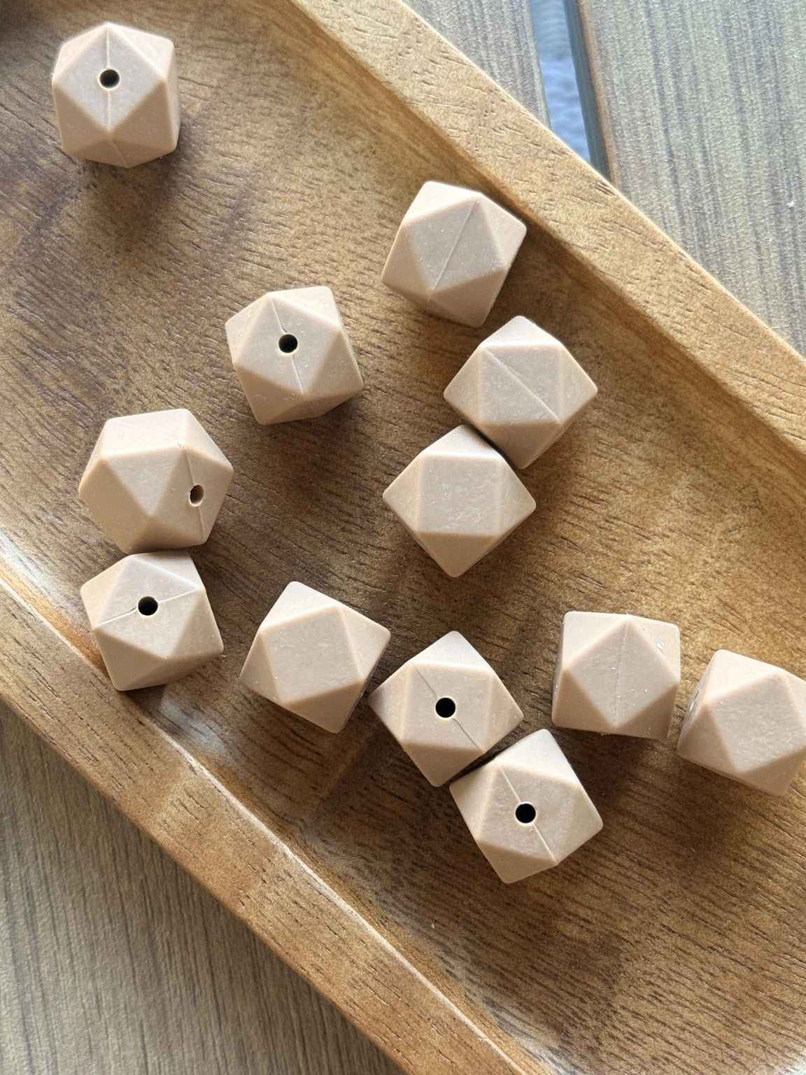 Desert Clay 14mm silicone hexagon beads displayed in a wooden tray. These faceted warm beige silicone beads are available in 5-count and 10-count bags for beadable pens, wristlets, keychains, badge reels, and DIY craft projects.