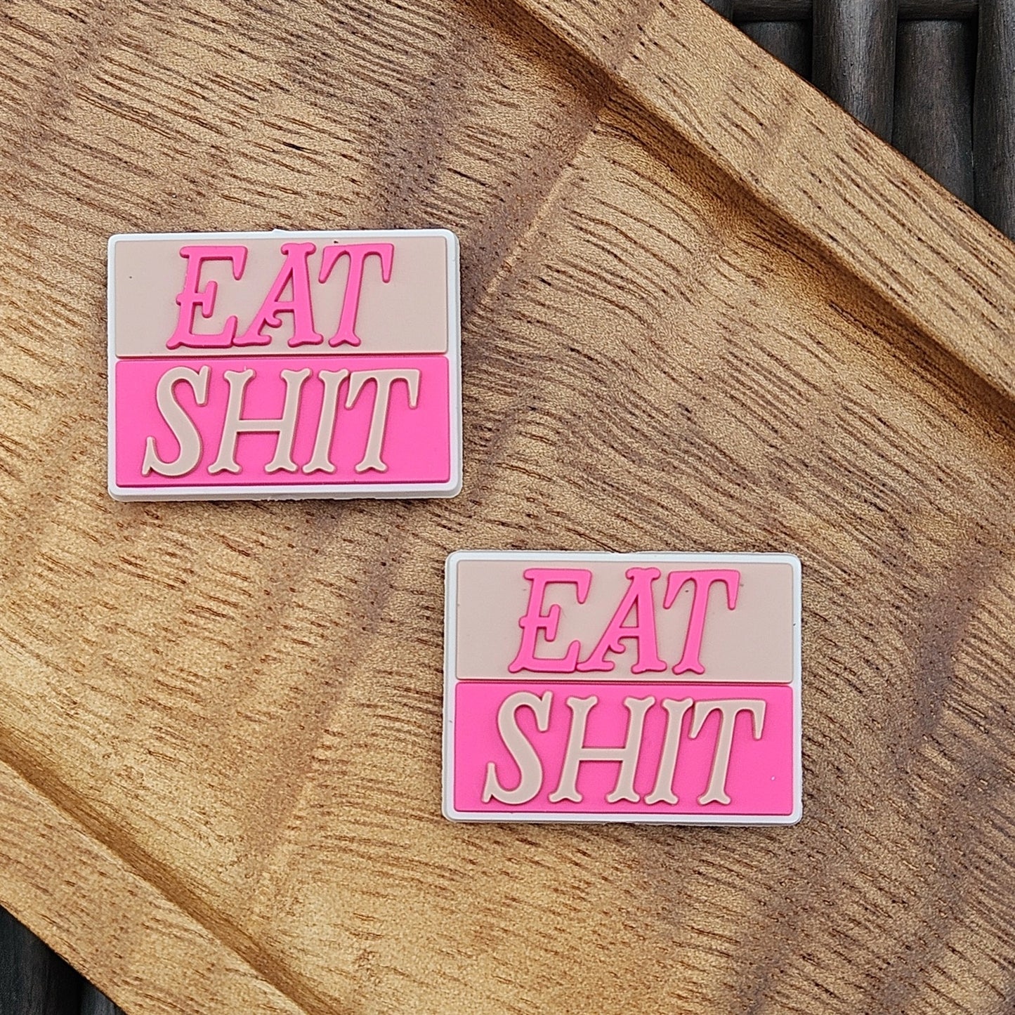 Funny adult humor silicone focal bead featuring the phrase “Eat Shit” displayed on a wooden tray. Perfect for beadable pens, keychains, wristlets, badge reels, lanyards, zipper pulls, and DIY crafting projects from Four Seasons of Happiness.