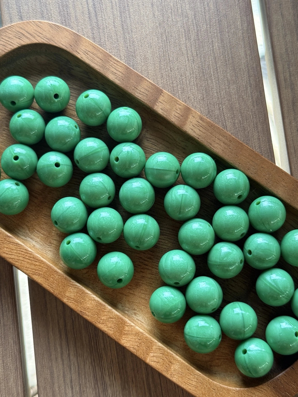 Glossy Emerald Lagoon Liquid Shimmer 15mm silicone beads from Four Seasons of Happiness displayed in a wooden tray. Premium food-grade silicone beads sold individually for beaded pens, keychains, wristlets, badge reels, jewelry making, and DIY craft projects.