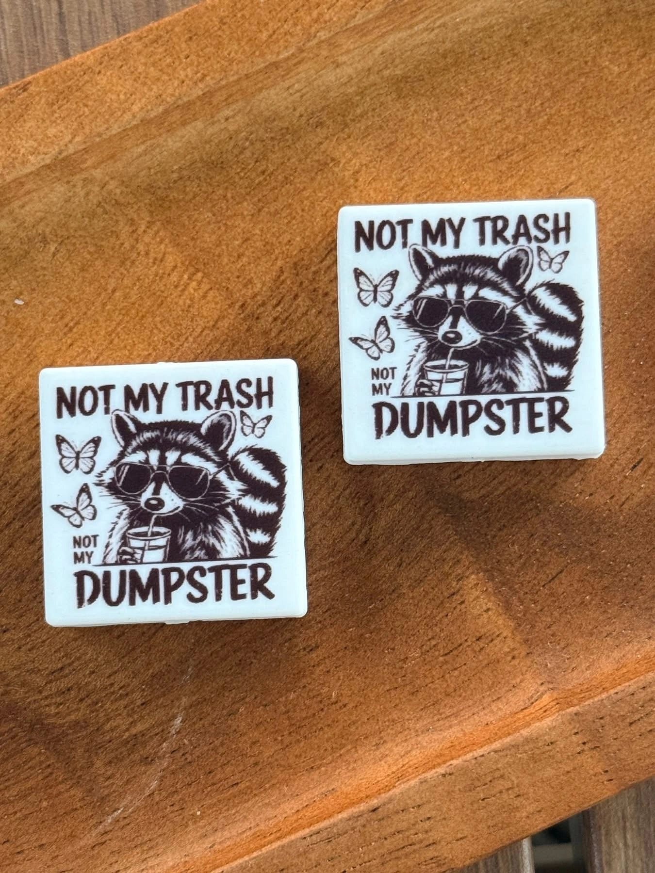 Funny raccoon silicone focal bead featuring sunglasses and the phrase “Not My Trash Not My Dumpster” displayed on a wooden tray for beadable pens, keychains, wristlets, badge reels, and DIY craft projects.
