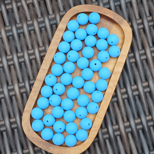 Ocean Current 15mm solid matte tropical blue silicone beads displayed in a wooden tray. Premium BPA-free craft beads for beadable pens, wristlets, keychains, badge reels, jewelry, and DIY handmade projects.