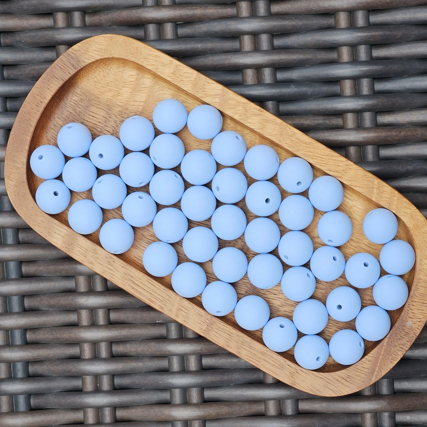 Serenity Sky 15mm solid matte silicone beads in a soft muted blue shade displayed in a wooden tray. Premium BPA-free craft beads for beadable pens, wristlets, keychains, badge reels, jewelry, and DIY handmade projects.