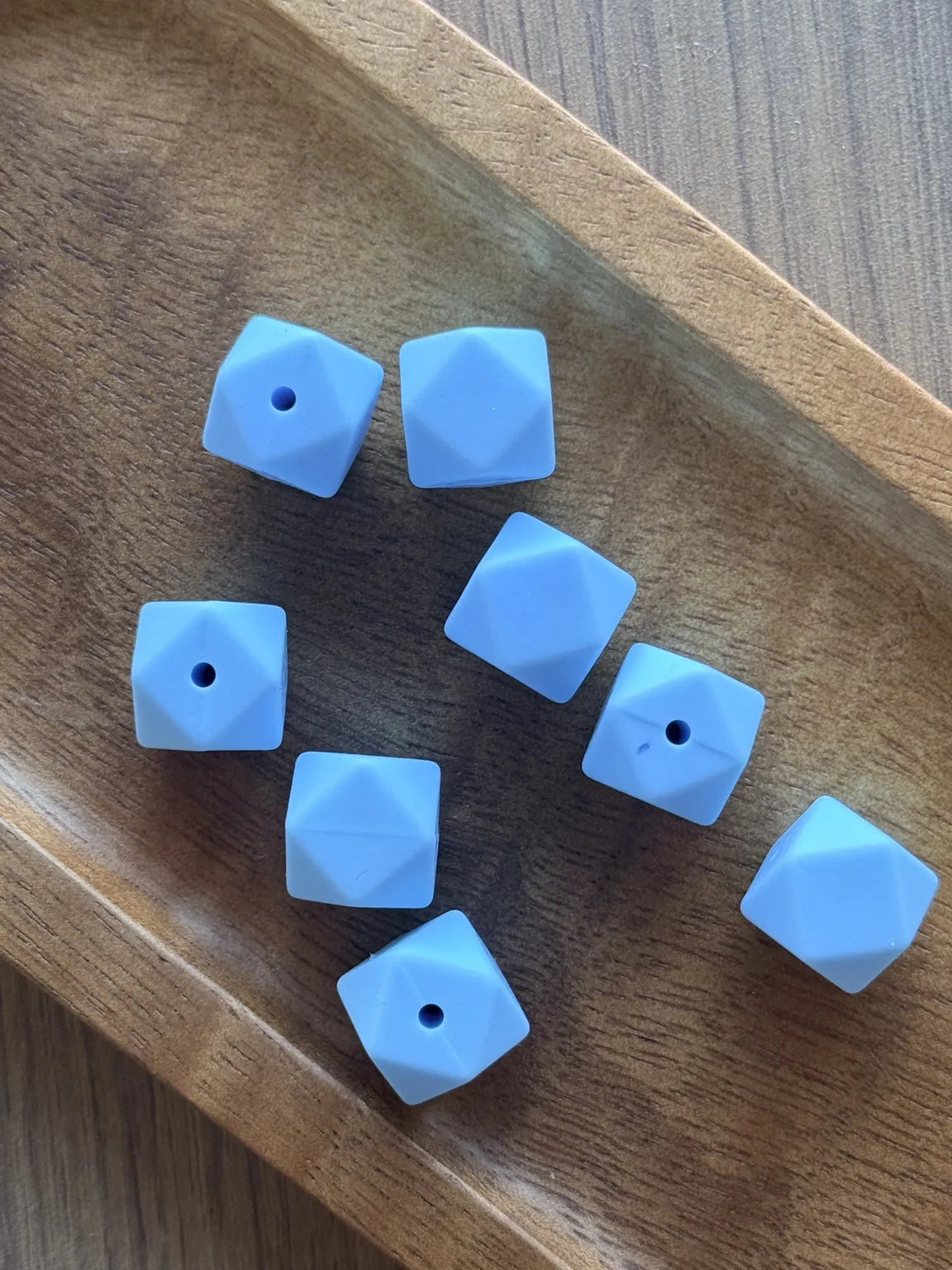     Pastel blue Sky Whisper 14mm silicone hexagon beads displayed in a wooden tray for DIY crafting projects.