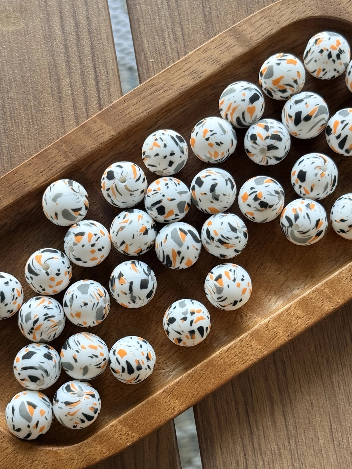 White 15mm silicone printed bead featuring orange, black, and gray terrazzo-style speckles for Halloween crafts, keychains, wristlets, badge reels, and beadable pens.
