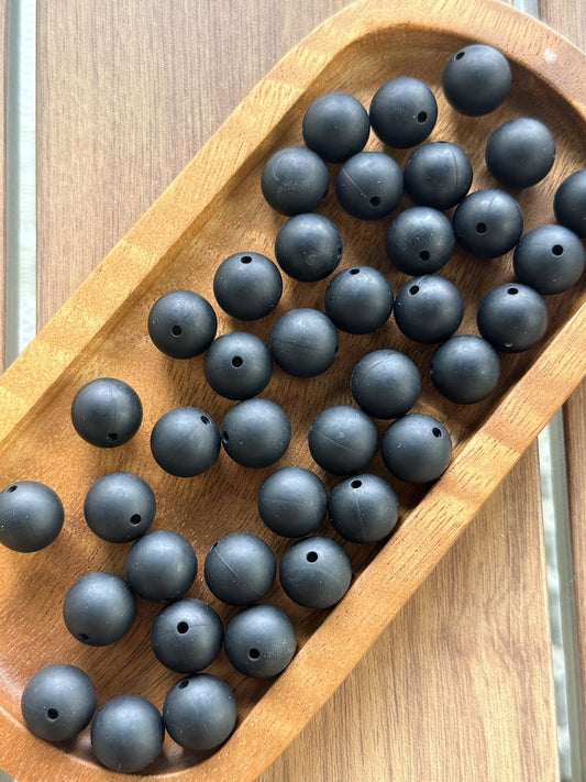 Black 15mm matte silicone round beads displayed in a wooden tray for crafting, jewelry making, beadable pens, wristlets, and DIY accessories.