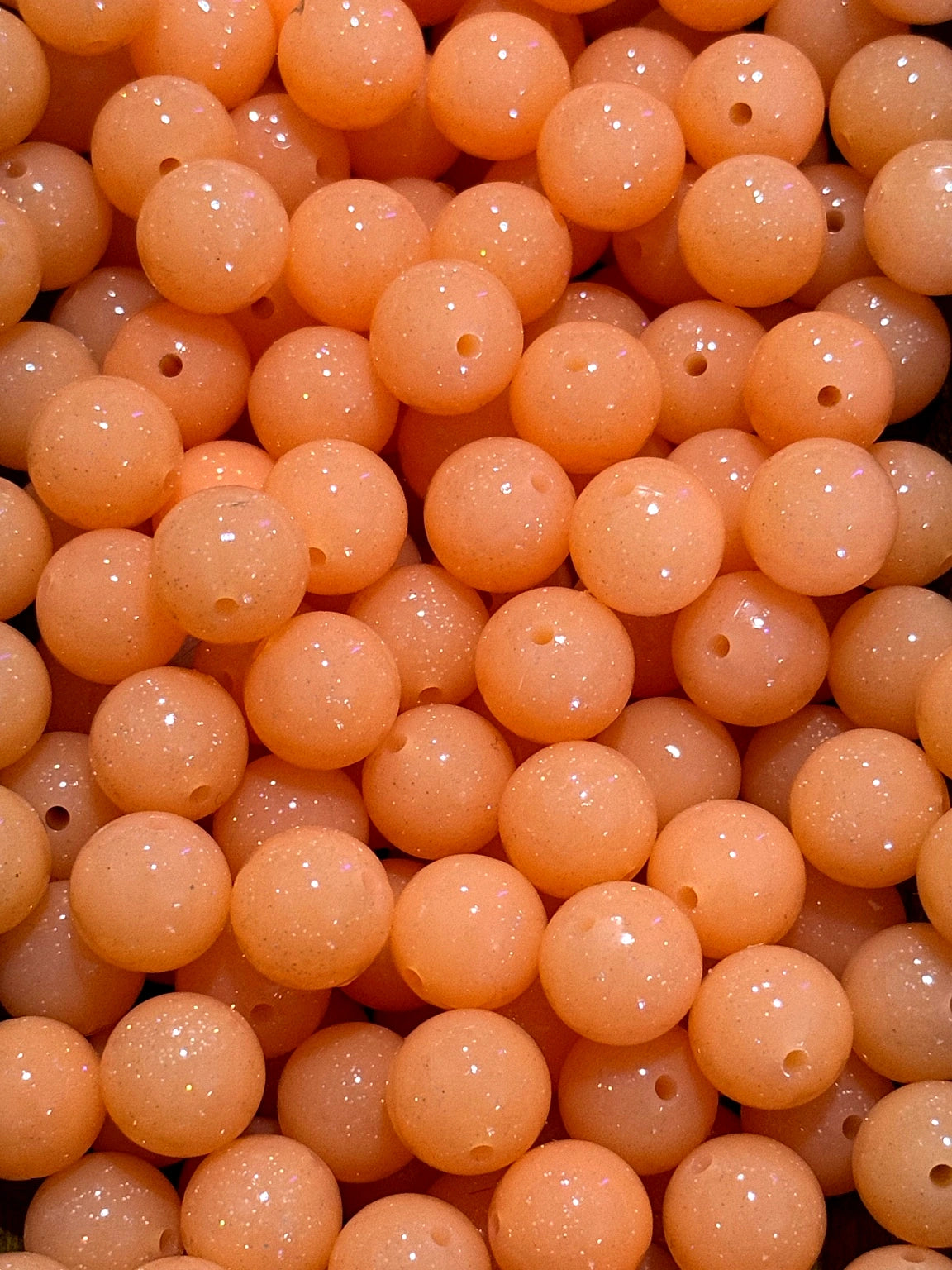 Close-up of peach-colored beads with holes, likely used for jewelry making.