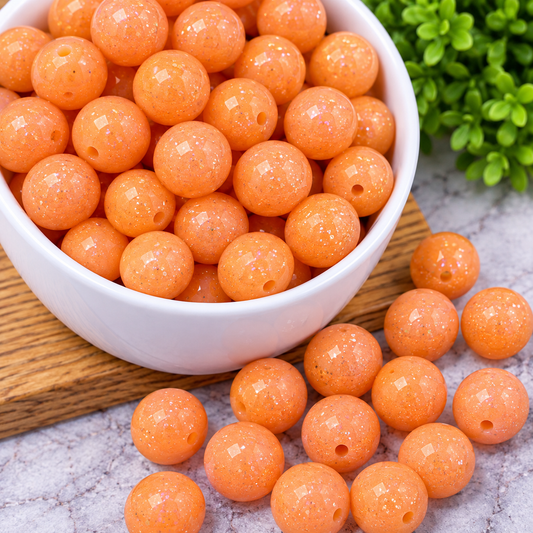 Orange glitter round beads with sparkling iridescent accents and center holes, displayed in a glass bowl for wristlets, keychains and DIY bead crafts.