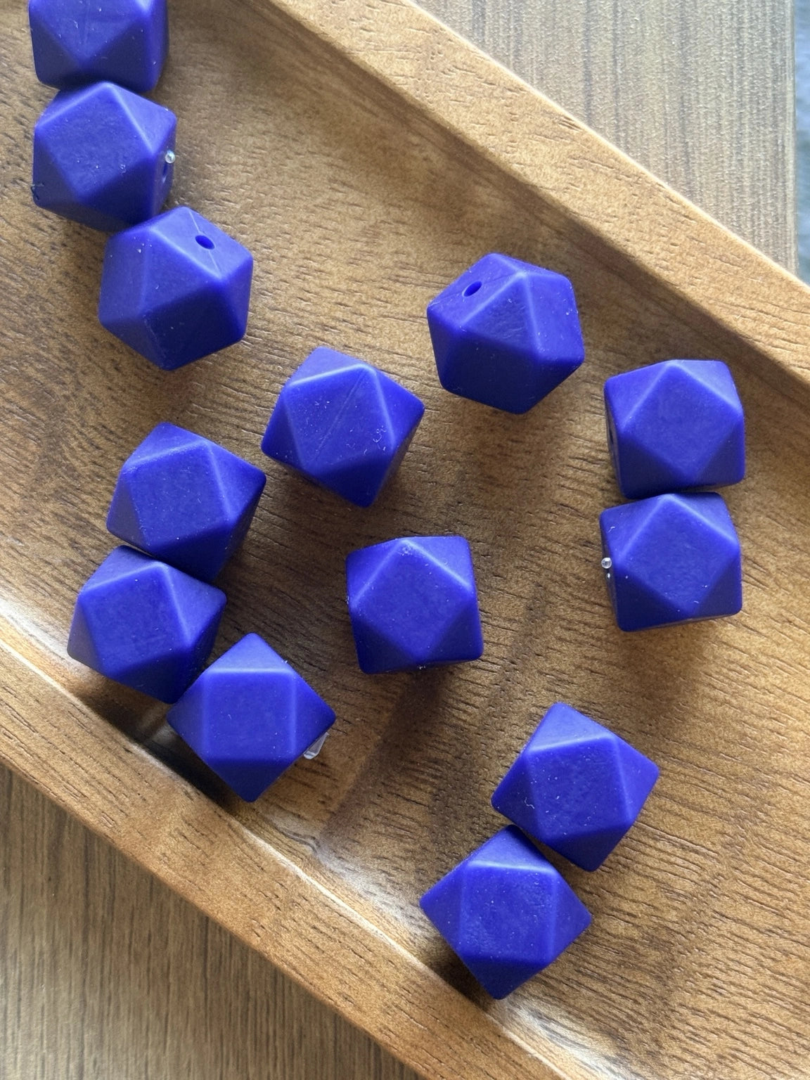 Sapphire Tide 14mm silicone hexagon beads displayed in a wooden tray. These faceted sapphire blue silicone beads are available in 5-count and 10-count bags for beadable pens, keychains, wristlets, badge reels, and DIY craft projects.