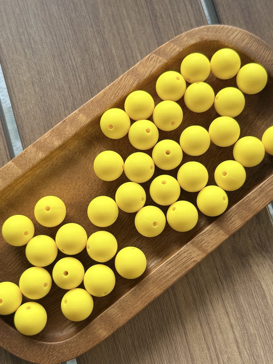 Bright yellow 15mm matte silicone round beads displayed in a wooden tray for crafting, pens, keychains, jewelry making, and beadable accessories.