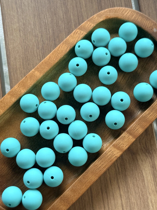 Bright turquoise teal 15mm matte silicone round beads displayed in a wooden tray for crafting, beadable pens, keychains, jewelry making, and DIY accessories.
