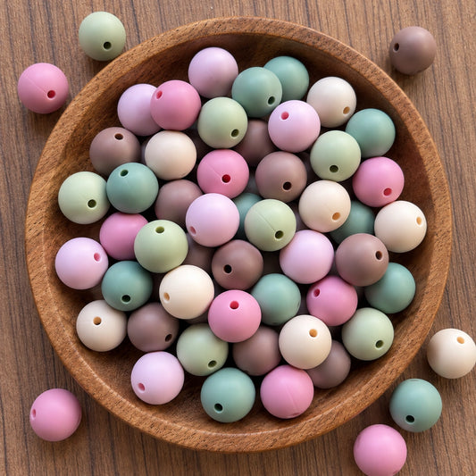 Whisper Of Happiness 15mm matte silicone bead mix in pink, brown, cream and green shades displayed in a wooden tray.